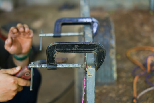 Metal clamp hand workshop repair tool metalwork Metal clamp securing steel bar in workshop while worker adjusts repair tool, highlighting practical craftsmanship and careful manual work