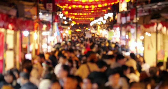 Packed crowd of shoppers is seen completely out of focus, walking past glowing market stalls and neon lights under rows of vibrant red lanterns on Dihua Street in Taipei. Shot with intentional defocus