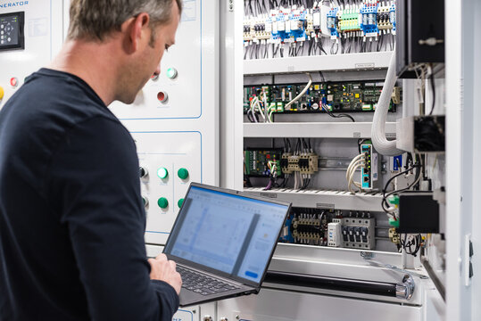 Caucasian Male Superyacht Chief Engineer - ETO working on the engine room control panel with laptop