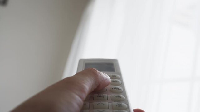 Close-up of hand controlling indoor climate with air conditioner remote, representing home comfort, temperature adjustment, cooling technology, modern living and household convenience