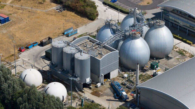 Aerial view of a modern industrial wastewater treatment facility with large silver spherical digester tanks and cylindrical storage silos in Reading, England, United Kingdom.