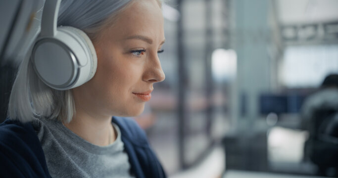 Portrait of a Focused Young Caucasian Woman Software Engineer With Silver Hair and White Headphones, Writing Program Code on Computer While Working on an App Project in an Office With a Diverse Team.