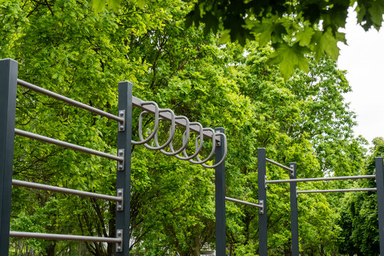 Outdoor calisthenics workout station with monkey bars and metal climbing equipment surrounded by lush green trees in public park. Concept of functional training, strength exercise and healthy lifestyl