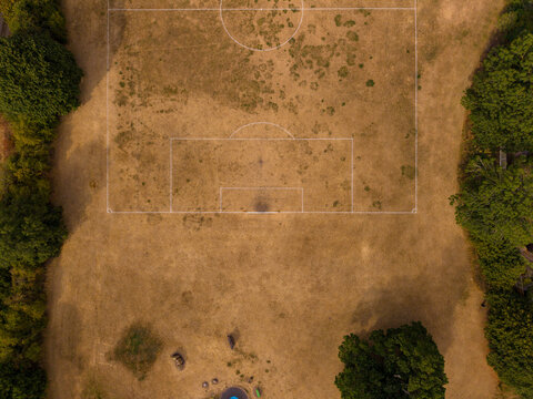 Aerial view of a dry, parched soccer field with white markings surrounded by lush green trees in Stafford, England, United Kingdom.