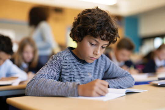 In a well-lit classroom, a young boy concentrates deeply on his writing, embodying the dedication and focus crucial for academic success and personal growth in children.