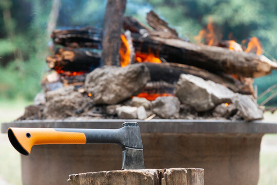 camping hatchet embedded in a wooden stump in front of a burning campfire in nature, concept of camping, concept of bushcraft, concept of survival