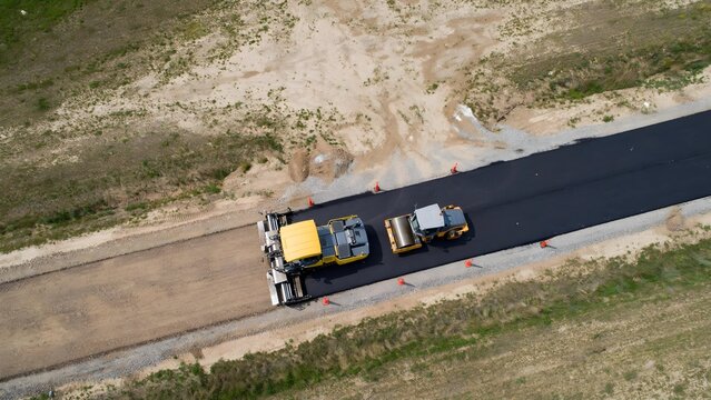 Aerial view of road construction with asphalt paver and roller machine laying new pavement.