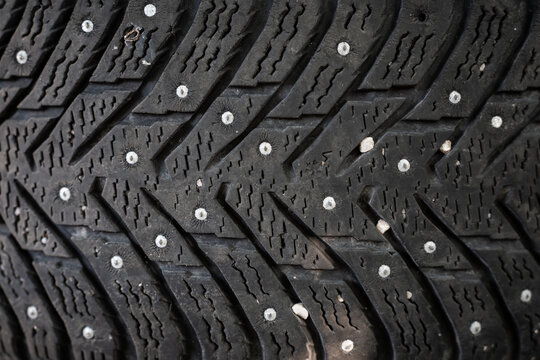 View of a close-up of a studded winter tire tread with metal studs and small pebbles embedded in the rubber grooves in Riga, Latvia.