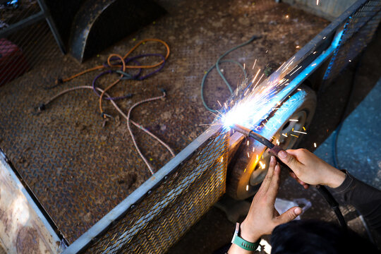 Welding torch metalwork spark worker steel fabrication process creates bright sparks while gloved artisan joins metal tubing dim industrial workshop, showing skilled craftsmanship and focused