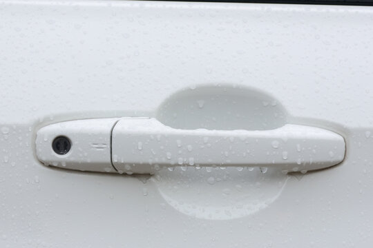 White car door handle with keyhole covered in rain droplets, showing wet automotive exterior and clean minimalist design