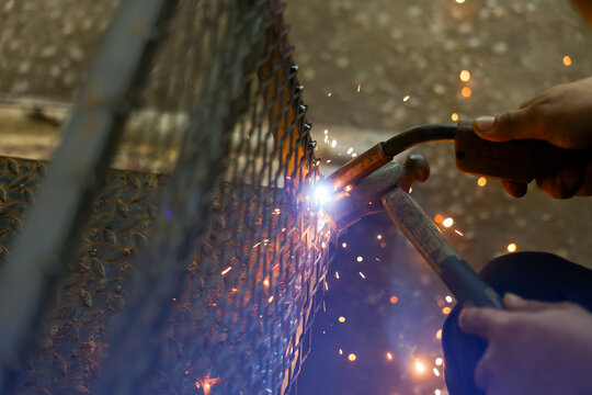 Welding torch and hammer repair metal mesh with bright sparks in dark workshop environment