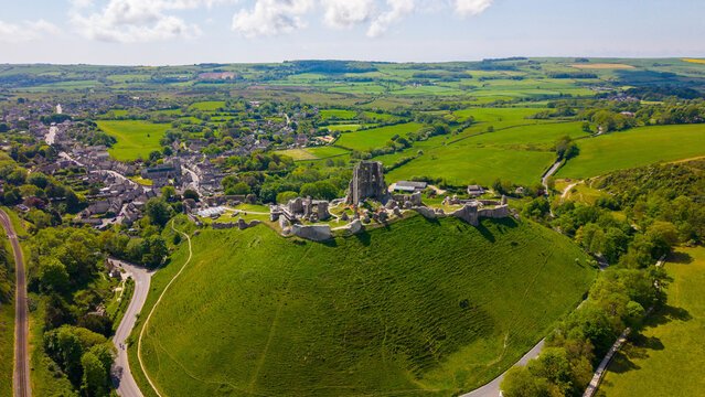 Aerial view of the historic ruins of Corfe Castle set atop a green hill overlooking the village and the surrounding Purbeck countryside in Corfe Castle, England, United Kingdom.