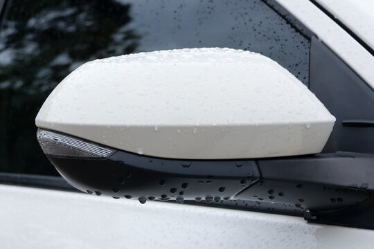 White vehicle side mirror with raindrop covered surface and reflective glass, captured in close up beside wet window during rainy weather