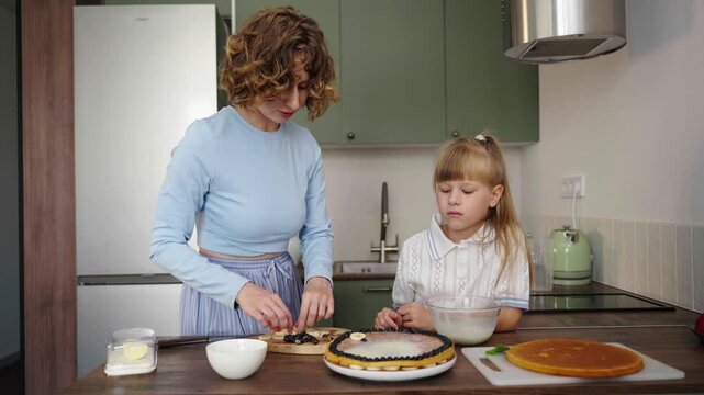 Mother and daughter bake layered cake together in cozy sunlit kitchen, 25 fps