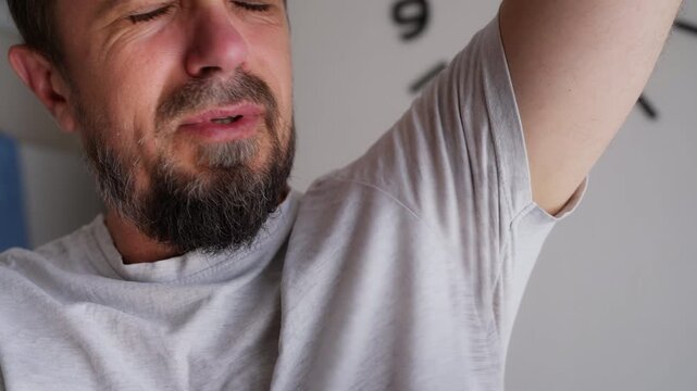 Disgusted bearded man checking his t-shirt for unpleasant sweat odor, highlighting underarm perspiration, body hygiene, deodorant use and everyday personal care