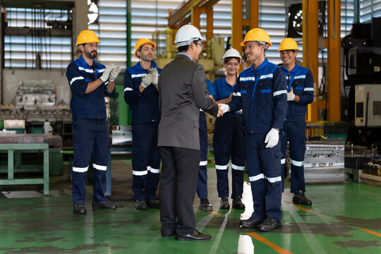 Factory manager shakes hands with an industrial worker while the production team applauds inside a manufacturing facility. Concept of teamwork, employee recognition, leadership, and workplace success