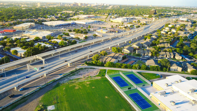 Vibrant blue sports courts, grassy athletic grounds border Loop 410 near Evers Road corridor. Educational campus fields frame high capacity transport arteries in San Antonio, Texas
