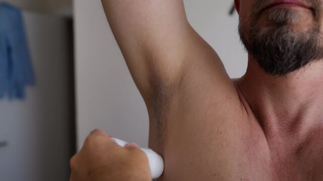 Close-up of bearded man applying roll-on deodorant to his armpit as part of a daily men's grooming routine, representing self care, hygiene and body odor prevention