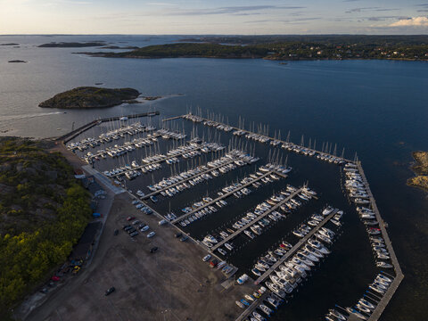 Aerial view of Sando marina with numerous sailboats docked in rows along the piers, surrounded by rocky coastline and calm waters in Vallda, Hallands lan, Sweden.