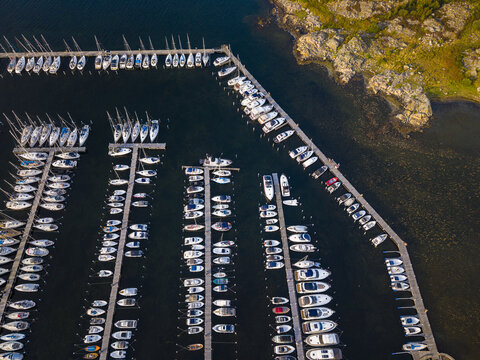 Aerial view of Sando marina with numerous sailboats moored at wooden piers along the rocky coastline in Vallda, Hallands lan, Sweden.