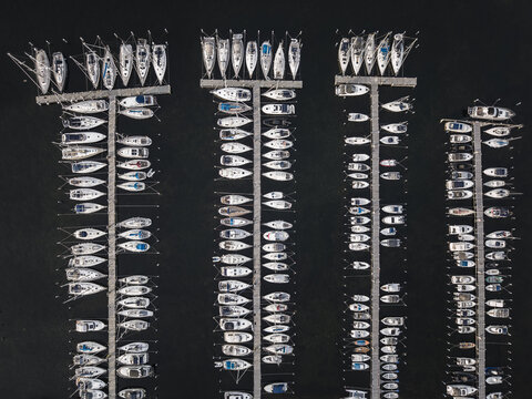 Aerial view of Sando marina with numerous sailboats and motorboats moored in orderly rows at wooden docks on dark water in Vallda, Hallands lan, Sweden.