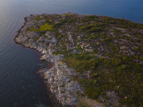 Aerial view of Sando island featuring rugged rocky coastline, lush green vegetation, and calm blue sea waters during golden hour in Vallda, Hallands lan, Sweden.