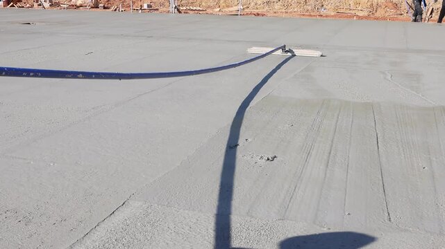 Workers are using broom tool to level wet concrete on construction site is residential area.
