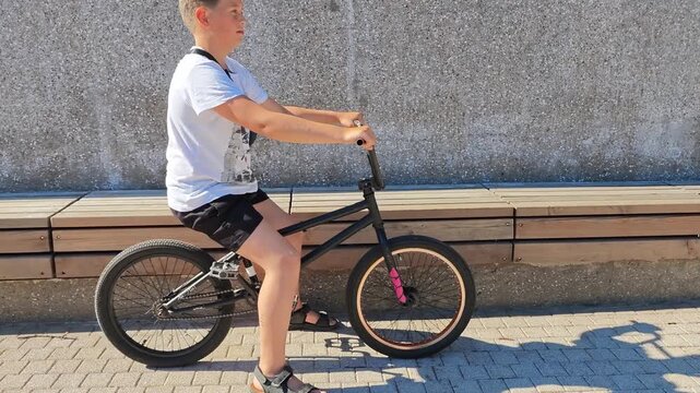 Boy rides a black bicycle on a sunny day in a city park, BMX