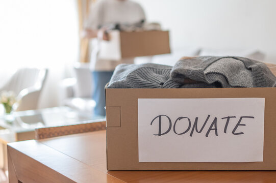 Person filling cardboard box with folded clothes and label donate for charity, decluttering, and giving, promoting help and reuse