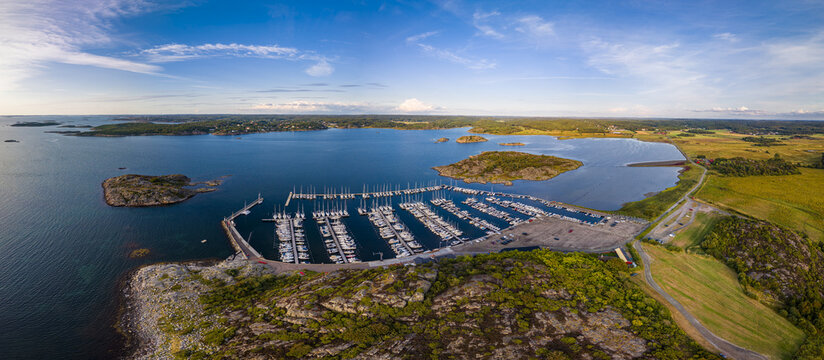 Aerial view of Sando marina with sailboats docked in the harbor, surrounded by rocky islands, coastal greenery, and blue sea under a clear sky Vallda, Hallands lan, Sweden.