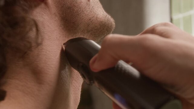 Cropped shot of unrecognizable young man shaving neck with electric trimmer in extreme close up. Footage is perfect for male grooming product ads and personal care marketing campaigns