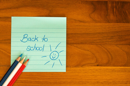 Concept de rentr&eacute;e scolaire avec des crayons de couleur et une note manuscrite &laquo; Back to school &raquo; sur un post-it vert, dispos&eacute;s sur un bureau en bois.