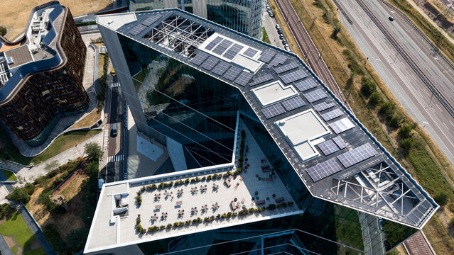 Aerial view of a modern office building featuring rooftop solar panels and sustainable energy infrastructure in an urban business area in Assago, Lombardy, Italy.