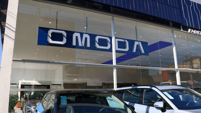 Fachada de concession&aacute;ria da Omoda com o logotipo da marca, vitrine envidra&ccedil;ada e ve&iacute;culos expostos, destacando o com&eacute;rcio automotivo na cidade do Alto Tiet&ecirc;. Mogi das Cruzes SP 10 Agosto 26
