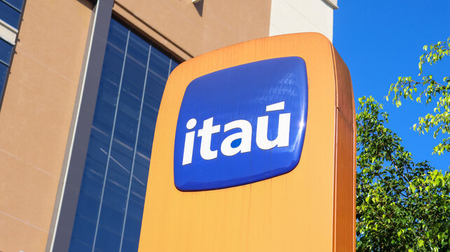 Placa externa com logotipo do banco Ita&uacute; instalada diante de edif&iacute;cio comercial e vegeta&ccedil;&atilde;o urbana, fotografada na cidade de S&atilde;o Paulo, SP, Brasil, em 10 de julho de 2026, sob c&eacute;u azul.