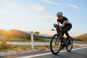Fototapeta premium Female Cyclist Training on Road Bike at Sunrise Along Country Road During Outdoor Endurance Ride