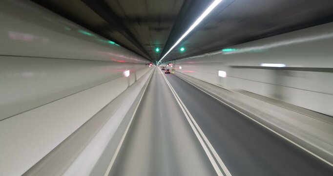Front view hyperlapse driving through underwater road tunnel in Hong Kong. Vehicle rushes through almost empty road with blurred white walls flashing around, while few cars pass by