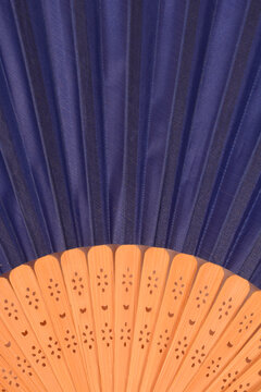 Close up view of an open oriental folding hand fan showing dark blue pleated fabric above light bamboo wooden ribs.