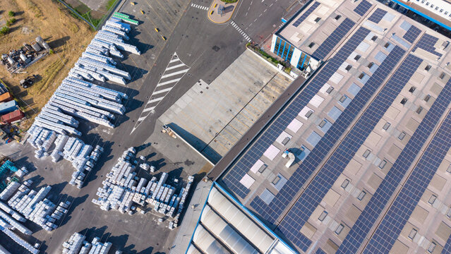 Aerial view of a construction materials manufacturing plant featuring a large roof covered in solar panels and rows of white bagged materials stored in the industrial yard in Milan, Lombardy, Italy.