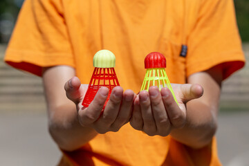 Fototapeta premium A boy holds two shuttlecocks of different colors in his palms for playing bambinton outdoors.