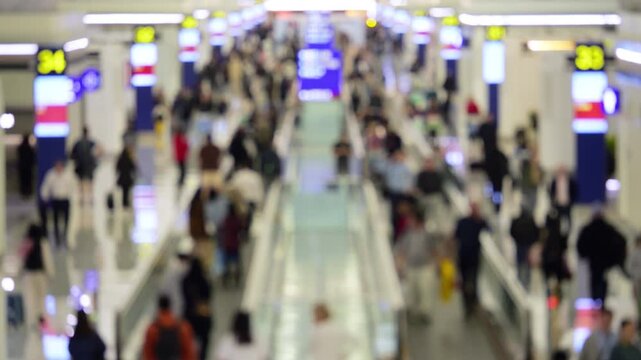 Lively flow of unrecognizable travelers streaks through massive public transit concourse during daytime time-lapse. This fast-moving, intentionally out-of-focus scene captures people flows