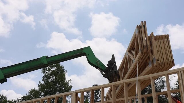 Machine lifts wooden trusses beams as workers assemble new building at construction site