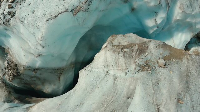 Closeup of glacier ice cave showing translucent blue ice, embedded rocks, shadowed crevices. Natural textures cool tones evoke cold, remote environment. Ideal for nature, climate, adventure themes