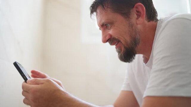 Man sitting on toilet and looking at smartphone with a suggestive and interested expression, illustrating private digital habits, online attraction and modern smartphone use