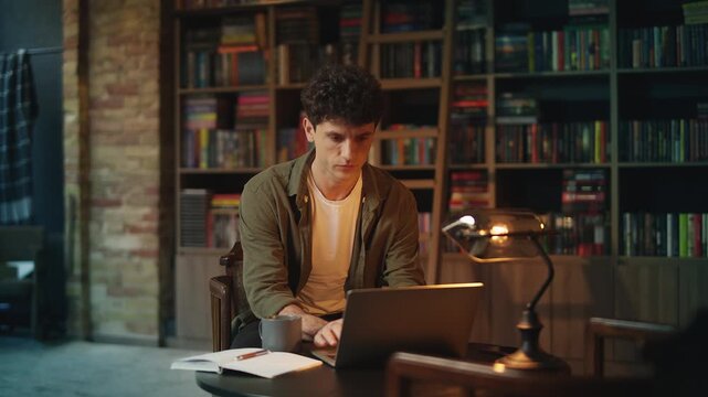 Young male author researches material for his new book on laptop in library
