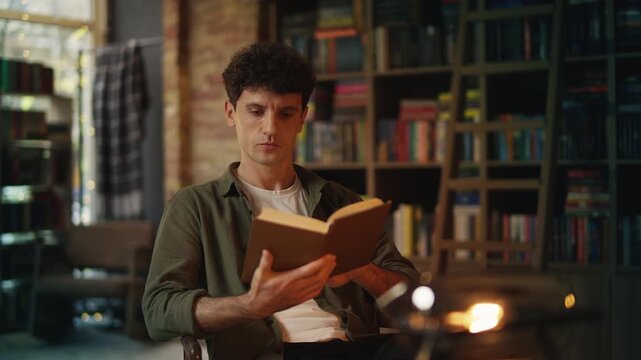 Focused young man reads book in library, enjoying literature and favorite hobby
