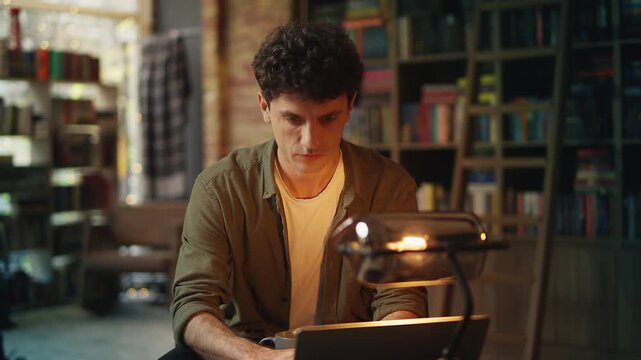 Male student researches scientific material on laptop in library, education