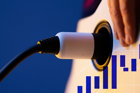 Charging connector seated in an electric vehicle port, featuring a matte finish and ribbed rubber, with digital financial charts for investment marketing