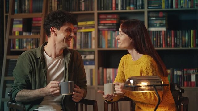 Happy young man and woman drink tea while talking in cozy coffee shop on date