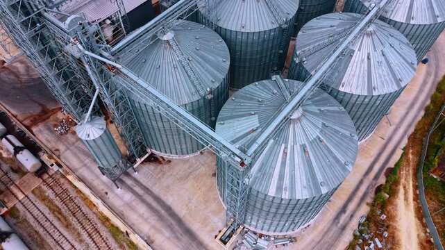 Large storage silos at a grain facility on a sunny day. These silos are used for grain storage in a large facility near train tracks.